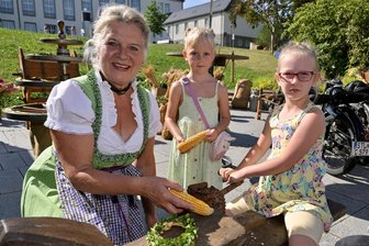 Herbstlicher Bauernmarkt lockt bei sommerlichen Temperaturen nach Oelsnitz - Sabina Tröger aus Oelsnitz (l.) hat der fünfjährigen Maila (Mitte) und der sechsjährigen Melina gezeigt, wie Maiskolben früher bearbeitet wurden.