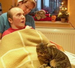 Hilfsprojekt in Westsachsen: Christian soll beweglich bleiben -
<p class="artikelinhalt">Christian Heymer mit Ergotherapeutin Nicole Nitzek und Katze Cassy bei Bewegungsübungen im Bett. </p>