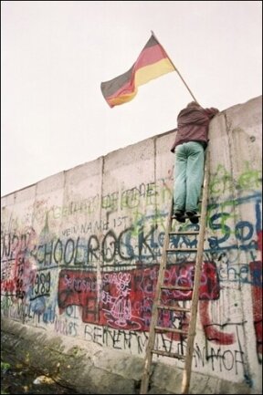 HINTERGRUND: Paris und London lehnten Vereinigung ab - Frankreich und Großbritannien haben damals zunächst ablehnend auf die deutsche Wiedervereinigung reagiert. Das Archivfoto zeigt einen Westberliner, der am 11. November 1989 eine bundesdeutsche Flagge über die Berliner Mauer reicht.