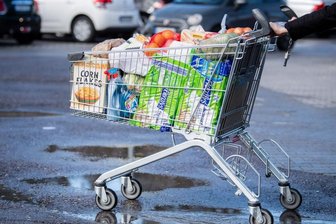 Ein Kunde schiebt einen bis zum Rand gefüllten Einkaufswagen über den Parkplatz eines Supermarktes.