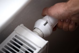 Ein Mann dreht am Thermostat einer Heizung.