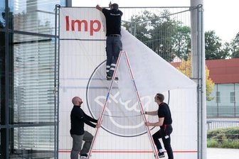 Arbeiter entfernen ein Transparent vor dem bisherigen Impfzentrum in Dresden.