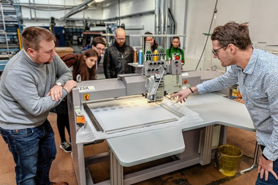In Reichenbach entwickelte Sensor-Matten sollen Pflegebetten revolutionieren - Forschungsingenieur Philipp Thiem (rechts) zeigt Teilnehmern des Akademiker-Tages, wie die neuartigen Drucksensoren mit einer Stickmaschine auf ein Gewerbe aufgebracht werden.
