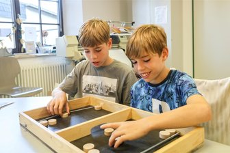 In Taura ist das Spielefieber ausgebrochen: Was ist Flitzpuck? - Lian (links) und Ayden Kaiser bereiten sich am Flitzpuck-Spiel auf die Meisterschaft am 30. September vor. Gewonnen hat, wer alle seine sechs Pucks im Gegnerfeld landet. Die Steine werden mit einem Gummi durch einen Tunnel geschnipst.