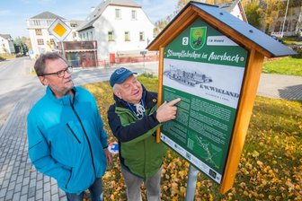 Infotafeln erinnern in Auerbach an 100-jährige Tradition - Der stellvertretende Bürgermeister Dieter Herold (links) und Christian Sehm, Vorsitzender des Heimatvereins Auerbach, die an einer der Geschichtstafeln an insgesamt sieben ehemaligen Strumpffabriken im erzgebirgischen Auerbach stehen. 