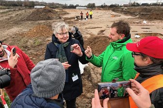 Karls Erlebnisdorf in Döbeln: Was gerade auf dem Baustellenareal passiert - Regina Smolnik, Landesarchäologin des Freistaats, erklärt Ministerpäsident Michael Kretschmer auf dem Gelände an der Autobahn 14 nahe der Abfahrt Döbeln-Nord, die Fortschritte bei den Ausgrabungenund zeigt einen der Funde, ein Steinbeil aus der Jungsteinzeit. 