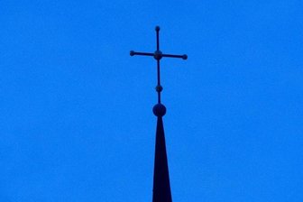 Ein Kreuz ist an einer Kirchturmspitze zu sehen.