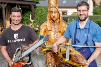 Kettensägenschnitzer laden auf Floßplatz - Mathias Kämpfer (links) hat schon etliche Kunstwerke per Kettensäge gezaubert - darunter den Bergmann (hinten) und das Modell des ADAC-Hubschraubers, den hier Muldenbergs Ortswehrchef Nils Golla hält.