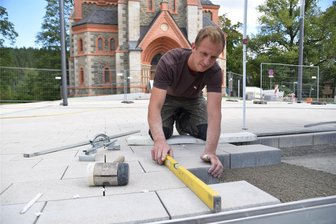 Kirchplatz-Bau in Bad Elster: Neues Wasserspiel soll zum Tag der Vogtländer sprudeln - Knochenjob bei Sommerhitze: Kevin Fischer und weitere Mitarbeiter vom Unternehmen Hoch-Tief-Landschaftsbau aus Schöneck bauen das Pflaster ein.