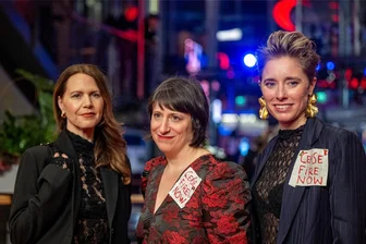 Kommentar zum Berlinale-Abschluss: Intellektuelle Bankrotterklärung - „Cease Fire Now“ steht auf den Kleidern von Eliza Hittman (M.) und Katrin Pors (r.), während sie zusammen mit Andrea Picard (l.) vor der Abschlussgala im Berlinale-Palast auf dem Roten Teppich stehen.