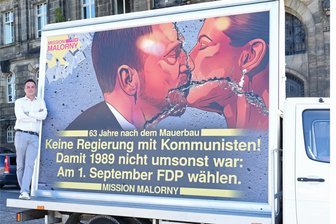 Kretschmer und Wagenknecht ganz innig: Wie Sachsens FDP den „sozialistischen Bruderkuss“ für den Wahlkampf neu interpretiert - FDP-Spitzenkandidat Robert Malorny mit dem auf einem Transporter montierten „Bruderkuss“-Plakat, das nur am Jahrestag des Mauerbaus durch Sachsen rollen soll. Ein ukrainischer Künstler hat der Partei das Motiv zur Verfügung gestellt.