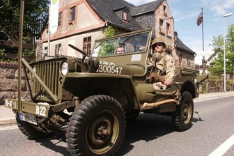 Kriegsende vor 80 Jahren im Erzgebirge: Granateneinschlag kostete vier Schönheider Jungs das Leben - Das einstige Haus Schönheider Hauptstraße 145/146, vor dem die Granate die vier Jungs in den Tod riss, bei der Passage eines Original-US-Jeeps aus dem Zweiten Weltkrieg während einer Oldtimer-Rundfahrt durch Schönheide.