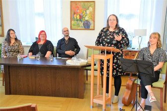 Kühn Fabuliertes kommt beim Publikum in Reichenbach an - Bevor es Ausschnitte aus den Büchern gab, hielt Grit Otto (stehend) einen Vortrag zu Fantasy-Literatur. Von links, sitzend: Kathrin Fuhrmann, Jessie Weber, Lyakon und Amy Seifert an der Gitarre.