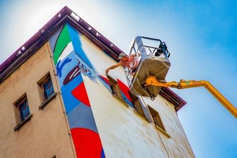 Künstler aus aller Welt in Flöha - Während ein Teil der 2021 geschaffenen Werke weiterhin bleibt, entstehen an anderer Stelle neue Bilder. Andreas Winter vom Mitarbeiterteam der Ibug bereitete am Freitag in luftiger Höhe eine Leinwand vor.