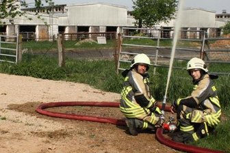 Kuhstallbrand: erste Übung nach Corona - Vize-Wehrleiter Steffen Pühler (l.) und Jugendwart Thomas Wendler sind während der Übung mit dem Schlauchverteiler beschäftigt. Im Hintergrund ist die ortsansässige Milchviehanlage zu sehen.