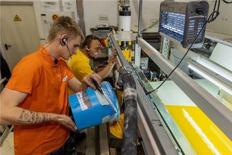 Kunstlederhersteller legt nach Corona-Flaute wieder zu - Bei Vowalon in Treuen wird nicht nur Kunstleder produziert, es werden auch Stoffe gefärbt. Hier bringen Marcus Haubold (hinten) und Tobias Beck Spezialfarbe in eine Beschichtungsmaschine ein.