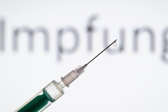 Eine Spritze wird vor den Schriftzug «Impfung» gehalten.