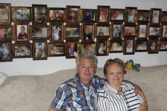 Lauterbacher Ehepaar: In 31 Jahren Adoptiveltern für 36 Kinder - Rosi und Peter Fischer vor den Fotos ihrer Pflege- oder Adoptivkinder, denen sie in schwierigen Zeiten als Pflegeeltern zur Seite standen. Die Gesichter der Kinder wurden von der Redaktion aus Gründen des Persönlichkeitsschutzes unkenntlich gemacht.