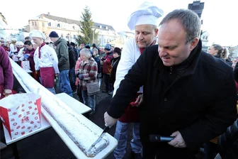 Leckerei für den guten Zweck: Der Marsch mit dem Riesenstollen zum Stollenmarkt in Brand-Erbisdorf - Oberbürgermeister Martin Antonow (r.) und Bäckermeister Dirk Selbmann schneiden den Riesenstollen an.