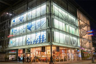 Leerer Kaufhof in Chemnitz leuchtet wieder – wer hinter den Grafiken an der Glasfassade steckt - So wird eine Buchillustration zu urbaner Kunst: Beleuchtete Auszüge aus der Kulturhauptstadt-Bewerbungsschrift kaschieren leeres Kaufhausgebäude.