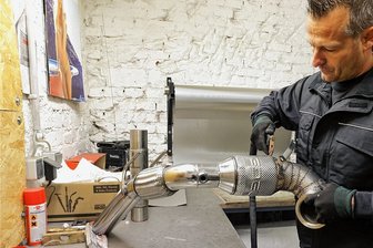 Lichtensteiner Tuner sind deutschlandweit zu hören - André Korb mit einer Downpipe, einer Verbindung zwischen Auspuff und Turbolader, für einen 7er Golf GTI. Das Firmenlogo ist gut sichtbar. Die Kunden sorgen mit Mund-zu-Mund-Propaganda für stetige Aufträge.