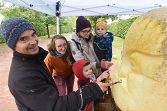 Lichtenwalde: Aus Riesen-Kürbissen werden Kunstwerke - Künstler ließen sich in Lichtenwalde gern über die Schulter schauen. Hesekiel auf dem Arm von Rahel und Balthasar mit Ida schauten zu, wie der Mondgeist entstand.
