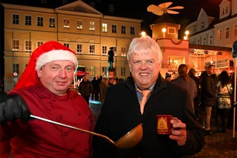 Linsen aus der Feldküche zum Weihnachtsmarkt in Hainichen - Der Weihnachtsmarkt in Hainichen ist eröffnet. Bei Matthias Preis vom Altstadtförderverein gibt es Linsen aus der Feldküche, OB Dieter Greysinger trinkt Glühwein aus einer Tasse mit dem Pyramidenmotiv.