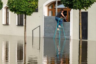 Liveblog zum Hochwasser in Deutschland: Lage in Bayern bleibt angespannt - Zwei Personen dichten in Passau den Eingang eines Cafés mit einer Hochwassersperre ab.