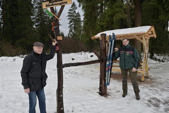 Loipe im Erzgebirge: Parkplatz kann jetzt doppelt so viele Autos aufnehmen - Gottfried Fuchs vom Verein Historische Skitruhe Schönheide (l.), der die Skier zur Dekoration bereitgestellt hat, und Revierförster Alexander Clauß auf dem erweiterten Parkplatz an der Loipe.