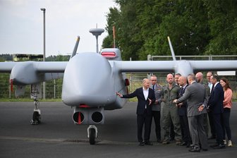 Luftfahrtmesse Ila in Berlin: Grünes Kerosin und olivgrüne Waffen - Bundeskanzler Olaf Scholz (SPD, links) steht beim Eröffnungsrundgang auf der Internationalen Luft- und Raumfahrtausstellung zusammen mit Militärs und Offiziellen neben einer Drohne Heron TP.