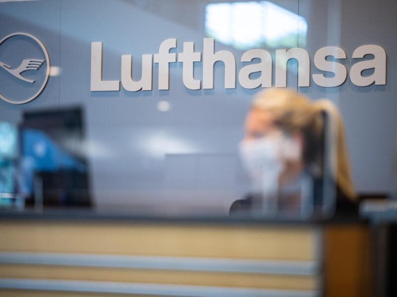 Lufthansa kündigt «Rückflug-Garantie» in Corona-Krise an -  
          Eine Mitarbeiterin der Lufthansa sitzt mit ihrer Mund- und Nasenschutzmaske am Check-in im Flughafen Münster-Osnabrück.