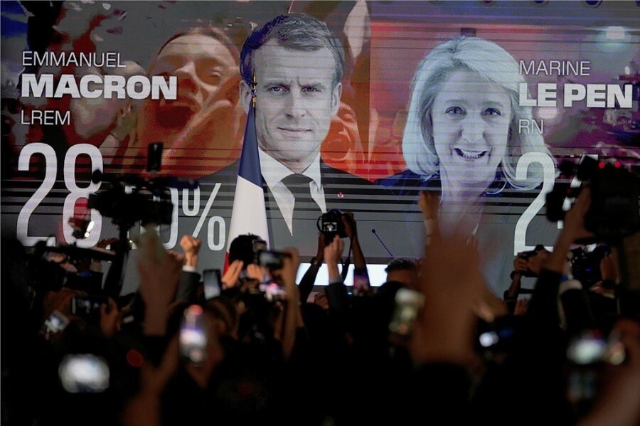 Macron und Le Pen in der Stichwahl: Frankreich vor einem Déjà-vu - Ein Bildschirm in Paris zeigt den französischen Präsidenten Macron und die rechtsextreme Kandidatin Le Pen am Wahltag.