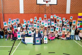 Malerei der Viertklässlerin Ida aus dem Erzgebirge ziert 61.000 Adventskalender in Sachsen - Die Grundschüler aus Niederwürschnitz halten stolz die Kalender mit dem Gewinnermotiv von Ida hoch, eines der abgebildeten Kinder. Bei der Preisverleihung dabei (vorn Mitte): Roland Warner, Vorsitzender der Geschäftsführung Eins Energie in Sachsen.