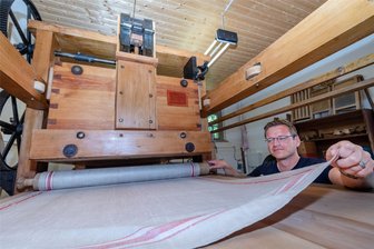 Markersdorf: Waschen wie vor 100 Jahren und was Radios mit Dampflokomotiven gemeinsam haben - Martin Bauch beim Einlegen eines Leinentuchs, zwischen dem die Wäschestücke in der Kaltmangel geplättet werden.