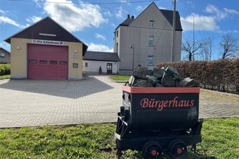 Mehr Platz für Feuerwehrleute und Einwohner: Was soll mit Bürgerhaus Schönbrunn passieren? - Das Bürgerhaus Schönbrunn (rechts) bildet ein Ensemble mit Eingang/Toiletten (Mitte) und dem Feuerwehrhaus. Vorn eine Lore als Symbol für den einst bedeutenden Schönbrunner Bergbau.