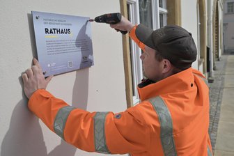 Mehr Service für Welterbe-Touristen: So setzt eine Stadt im Erzgebirge ihre Sehenswürdigkeiten in Szene - Kevin Schmuck, Mitarbeiter des Betriebshofs, bringt das neue Schild am Rathaus an.
