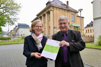 Millionenprojekt im Erzgebirge: Frühere Freimaurerloge wird zum „Hochzeitspalast“ - Regina Kraushaar, die Präsidentin der Landesdirektion Sachsen, hat OB Heinrich Kohl den Fördermittelbescheid für die Sanierung des Clemens-Winkler-Clubs (im Hintergrund) in Aue übergeben.