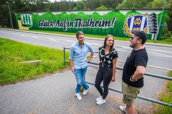 Mit „Glück auf“-Spruch und FCE-Logo: Fanszene von Erzgebirge Aue sprüht riesiges Graffiti an Thalheimer Bauhof - Bürgermeister Nico Dittmann, Pressesprecherin Michele Fankhänel und Max vom Verein Block P (v. l.) freuen sich über das neue Kunstwerk am Ortseingang von Thalheim.