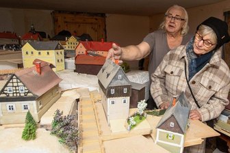 Modell des versunkenen Ortes Pöhl soll in ein eigenes Gebäude ziehen - Holzkünstler Jens Weber öffnete am Samstag sein Haus für Interessierte. Margitta Römer erklärt er die bereits fertiggestellten Modellhäuser des alten Dorfes Pöhl. Ein Verein will dem Modell nun eine Heimat geben.