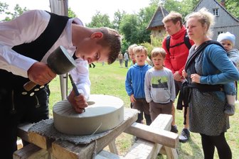 Mühlentag im Landkreis Zwickau: Junger Steinmetz zieht Blicke auf sich - Die Familie von Melanie Rothe aus Gera beobachtet genau, wie Steinmetzlehrling Frank Falke die Rillen in den Mühlstein schlägt.