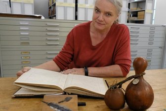 Museum Burg Mylau: Herkunft von 80 Afrika-Objekten unklar - Museumsleiterin Sina Lorbeer-Klausnitz mit einem Inventarbuch des Naturkundevereins Mylau, Messerklinge und Pfeilspitze der Herero aus dem heutigen Namibia sowie Flaschenkürbis-Gefäßen aus Westafrika. 
