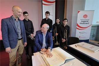Musikwettbewerb: Ein Präsident besucht Meerane - Martin Maria Krüger trägt sich ins Goldene Buch ein. Rathauschef Jörg Schmeißer (l.) und Schüler schauen zu.
