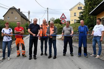 Nach fast drei Monaten Bauzeit: Elsterberger Straße in Scholas freigegeben - Mit Baubeteiligten und Bürgern geben Ortsvorsteher Uwe Pansa (links) und Bürgermeister Axel Markert mit einem „Scherenschnitt“ die Straße frei.