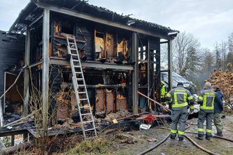 Nach verheerendem Großfeuer im Erzgebirge: Bürgermeister bietet Brandopfern sein Ferienhaus an - Polizei, Feuerwehr und eine Bewohnerin stehen vor den Überresten des abgebrannten Wohnhauses in Wilischthal.