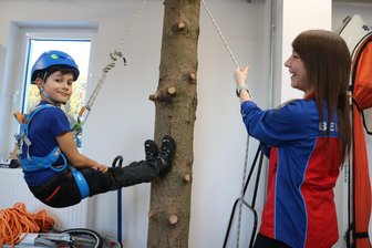 Nachwuchsretter im Erzgebirge können mit neuer Ausrüstung entspannt am Baumstamm hängen - Eddie (9) probiert die neue Ausrüstung am Kletterbaum aus. Jessica Cristescu (r.) sichert ihn.
