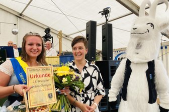 Nächste Gemeinde im Erzgebirge sagt ihr Volksfest für dieses Jahr ab: Das sind die Gründe - Wurzelkönigin Leonie Joyce Schmidt (l.), hier mit Bürgermeisterin Franziska Meier und Orts-Maskottchen Geißbock Hansi, muss bis 2026 auf ihren nächsten Auftritt beim Bockauer Wurzelfest warten.