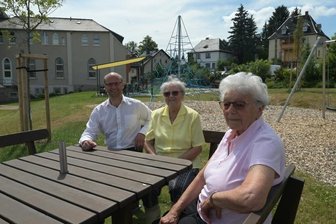 Neu gestalteter Kirchengarten verbindet Generationen - Michael Kropff, Pastor der Evangelisch-methodistischen Kirche in Zschorlau (li.) hat sich mit Irmtraud Friedrich (Mitte) und Helga Meier zusammengesetzt. Die beiden Bewohnerinnen des Seniorenparks genießen das schöne Wetter im neu gestalteten Kirchengarten.