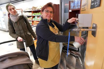 Neue Milchtankstelle in Freiberg: Wo in Mittelsachsen frisch gezapfte Milch verkauft wird - Im Bioladen „Vorwerk Podemus " in der Korngasse in Freiberg zeigt Marktleiterin Katrin Claus, wie das Milchzapfen funktioniert. Stammkundin Lisa Metzler aus Freiberg schaut ihr dabei zu.