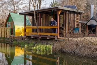 Neue Öko-Uferhütte im Vogtland sucht Test-Bewohner - Haustechniker Mirko Buschner an der mit Daniel Glaw erbauten Uferhütte. Links das Kinder-Schlafiglu, rechts der innovative Grill-Kamin. Über einen von der Schlosserei Fleischmann gebauten Wärmetauscher wird Luft eingesaugt und via Rohr in die Hütte zum Heizen geleitet. Die Öko-Immobilie verfügt über einen separaten Zugang und Sonnenplatz.