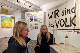 Neue Sonderausstellung in Zschopau: Wie eine Babyflasche die Wende 1989 greifbar macht - Lehrerin Stephanie Seidel (links) und Stadtmitarbeiterin Judith Hauße vor der Babyflasche, die an die Wende-Geschichte einer jungen Mutter erinnert.